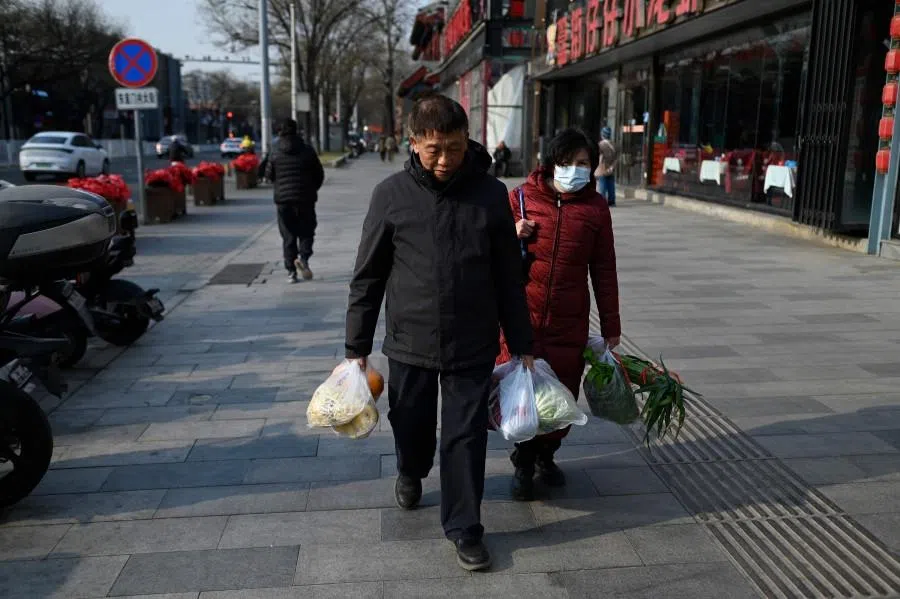An elderly man and woman walk with their groceries past a restaurant in Beijing on 22 December 2025. (Wang Zhao/AFP)
