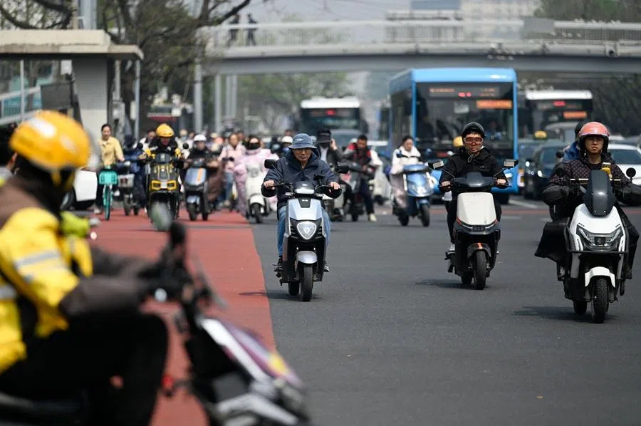 People riding electric bicycles cross a street in Beijing, China, 15 April 2026. (Wang Zhao/AFP)