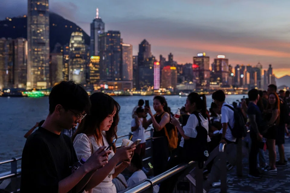 Tourists rest by the waterfront in Tsim Sha Tsui, with Hong Kong’s financial district visible in the background in Hong Kong, China, on 23 July 2024. (Tyrone Siu/Reuters)