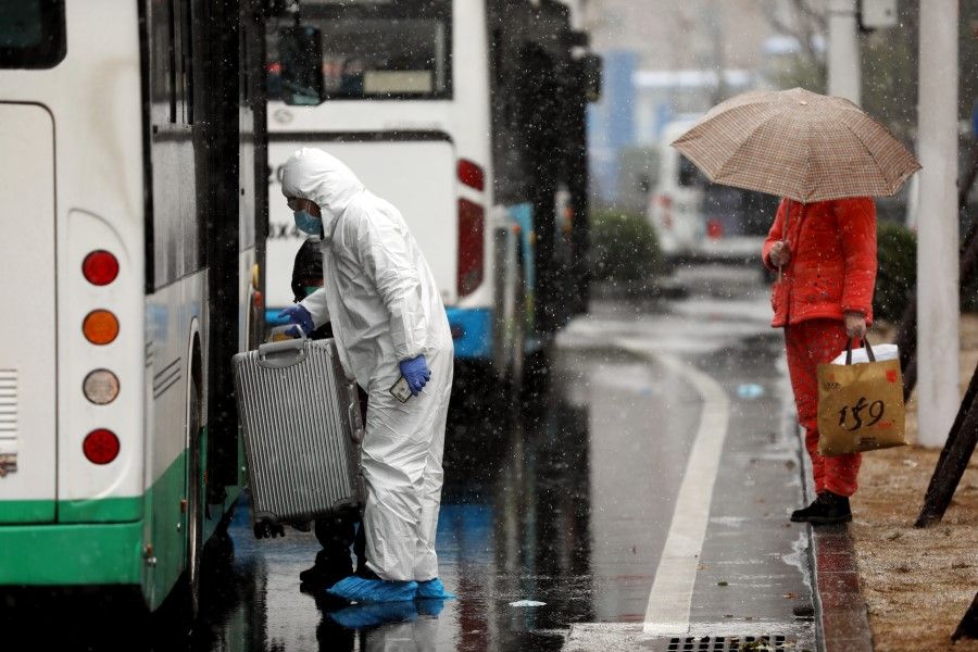 A worker in protective suit lifts a suitcase from a bus amid snow to help transport Covid-19 patients outside a hospital in Wuhan. (China Daily via REUTERS)