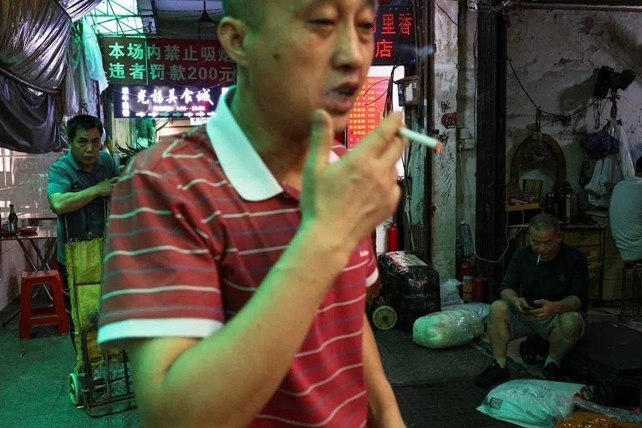 A person smokes a cigarette in an alley in a clothing wholesale district in Guangzhou, Guangdong province, China, 15 April 2026.