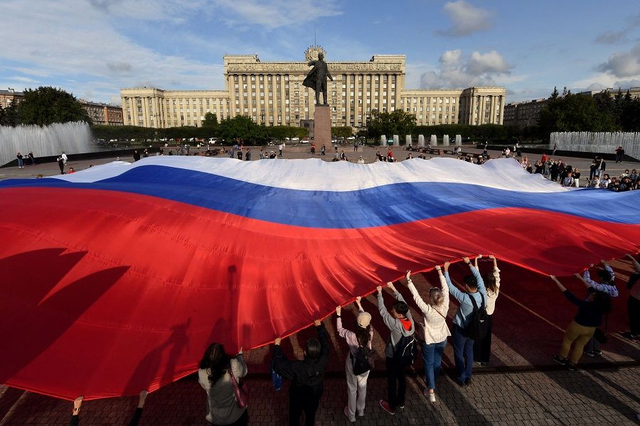 People hold a giant Russian flag in front of a statue of the founder of the Soviet Union Vladimir Lenin and the House of Soviets during Russia's National Flag Day celebrations in the Moscow Square in Saint Petersburg, Russia, on 22 August 2023. (Olga Maltseva/AFP)