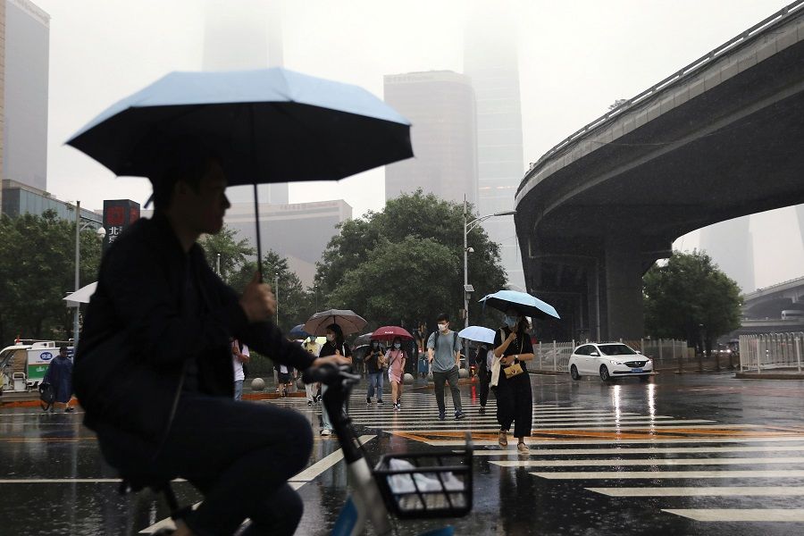 People are seen amid heavy rainfall during morning rush hour in Beijing's Central Business District, China, 12 July 2021. (Tingshu Wang/Reuters)