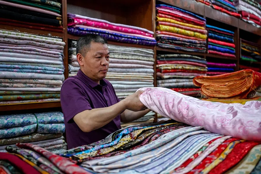 A vendor folds silk and other fabric in a textile market which sells to the domestic market as well as for export, in Shaoxing, in China’s eastern Zhejiang province on 9 May 2025.  (Greg Baker/AFP)