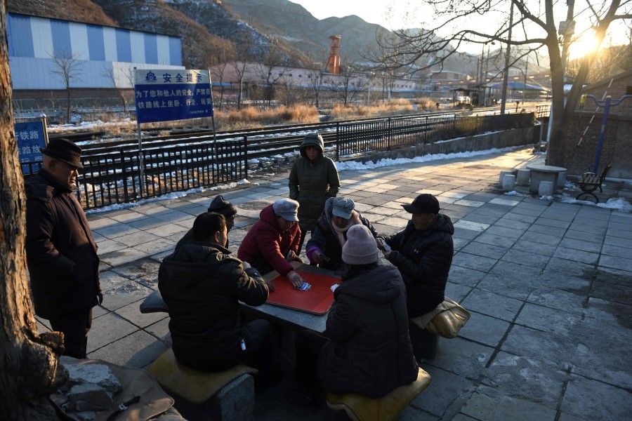 Residents playing cards in their village outside the Datai coal mine (at rear) in Mentougou, west of Beijing, 8 January 2020. (Greg Baker/AFP)