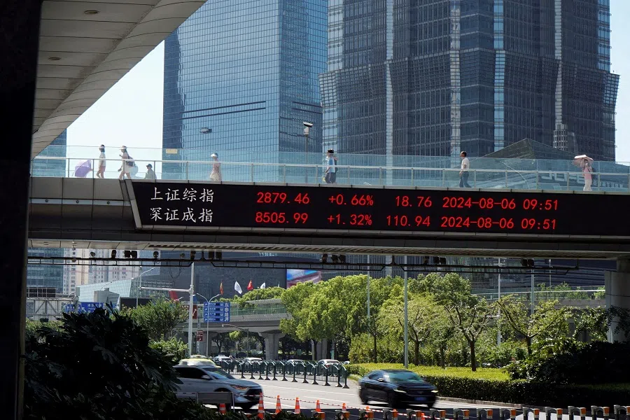People walk on an overpass with a display of stock information in front of buildings in the Lujiazui financial district in Shanghai, China, on 6 August 2024. (Nicoco Chan/Reuters)