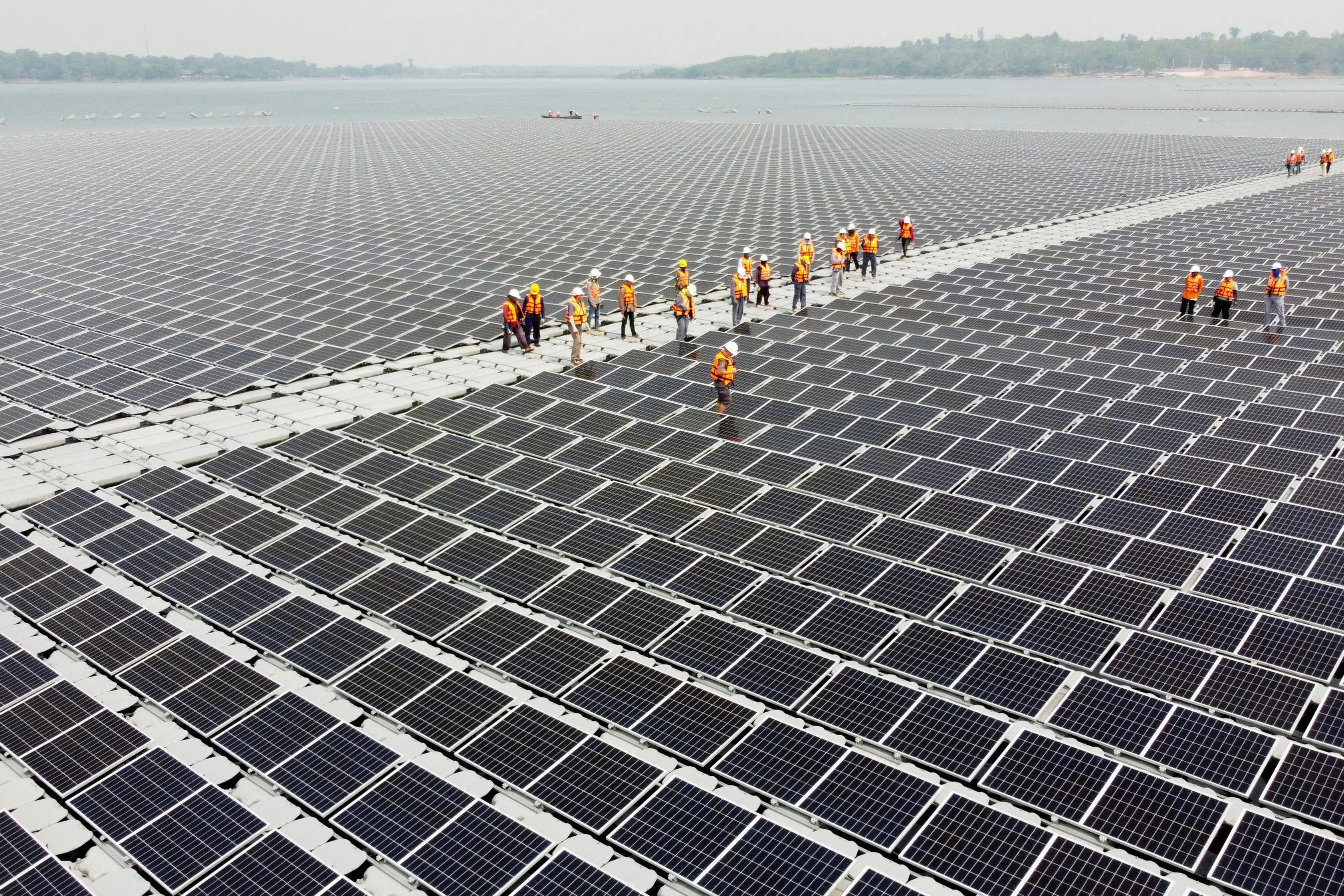 Workers walk between solar cell panels over the water surface of Sirindhorn Dam in Ubon Ratchathani, Thailand, on 8 April 2021. (Prapan Chankaew/Reuters)