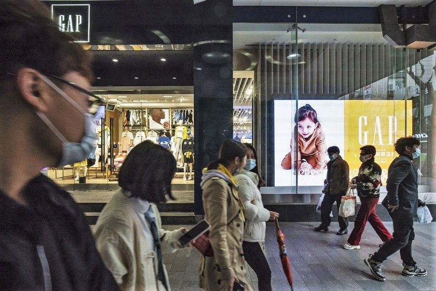 Pedestrians wearing protective masks walk past a Gap Inc. store in Shanghai, China, 9 March 2021. (Qilai Shen/Bloomberg)