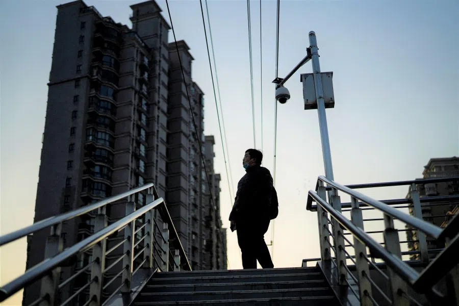 A pedestrian stands on an overpass near residential buildings and a surveillance camera, in Shanghai, China, on 24 February 2022. (Aly Song/Reuters)