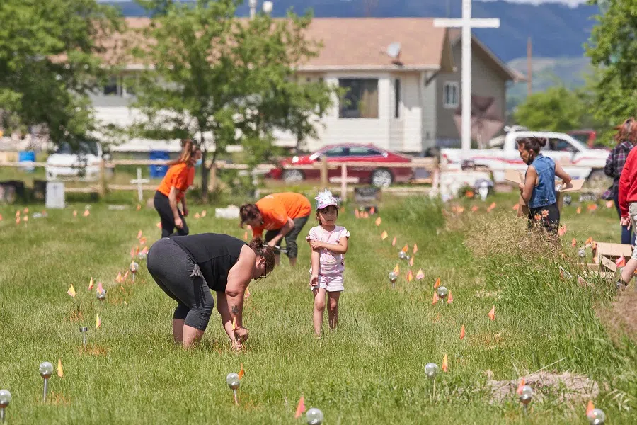 Members of the community place solar lights next to the flags which mark the spots where remains were discovered by ground penetrating radar at the site of the former Marieval Indian Residential School on the Cowessess First Nation in Saskatchewan, Canada, on 26 June 2021. (Geoff Robins/AFP)