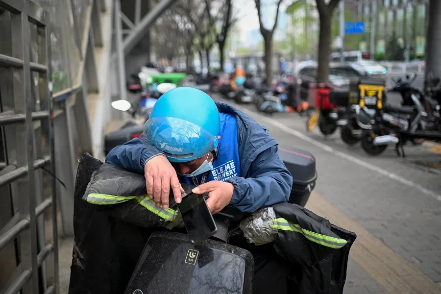 A food delivery worker rests on his electric bicycle by a roadside in Beijing, China, on 1 April 2023. (Wang Zhao/AFP)