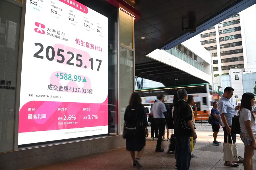Pedestrians walk past a sign showing the numbers of the Hang Seng Index in Hong Kong on 27 September 2024. (Peter Parks/AFP)