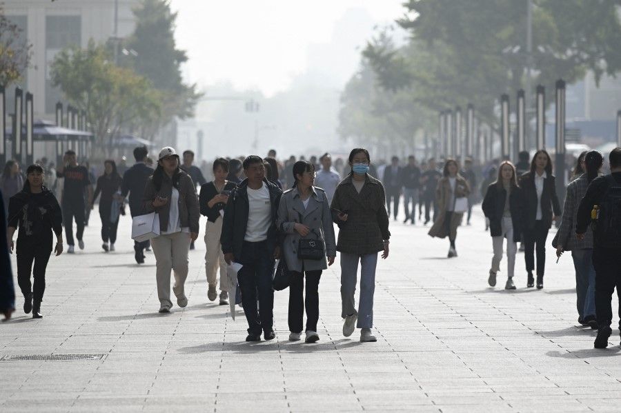 People walk along a business street in Beijing on 31 October 2023. (Wang Zhao/AFP)