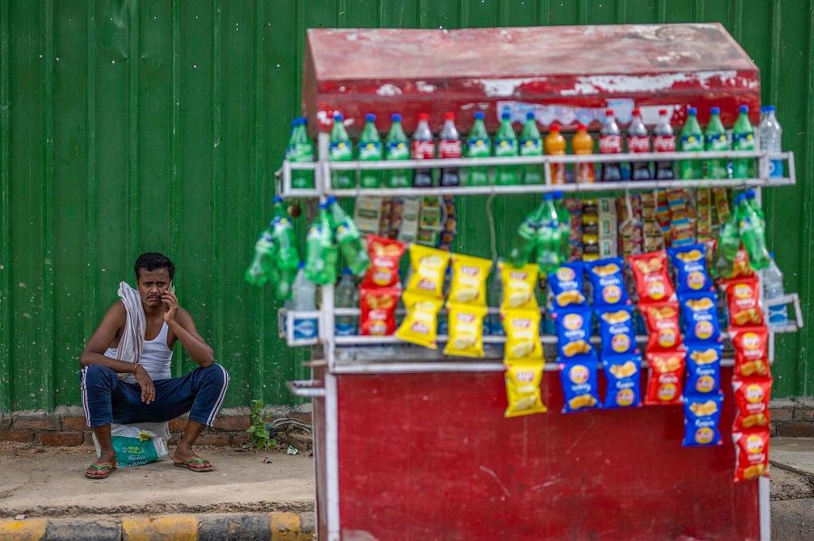 A man selling soft drinks and snacks on a cart speaks on his mobile phone while waiting for customers along a street in New Delhi, India, on 2 June 2022. (Jewel Samad/AFP)