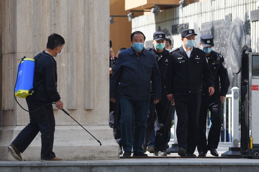 Police and officials emerge from a high school as a man (L) disinfects the entrance after students arrived for their first day of classes in Beijing on 27 April 2020. (Greg Baker/AFP)