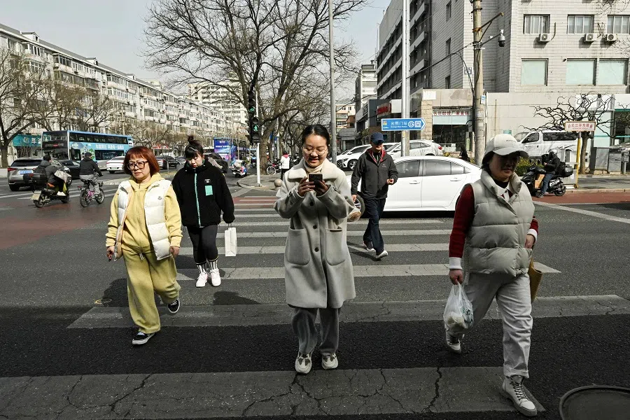 This photo taken on 13 March 2025 shows student Liu Yuxuan (C) playing “Love and Deepspace” game while walking along a street in Beijing. (Adek Berry/AFP)