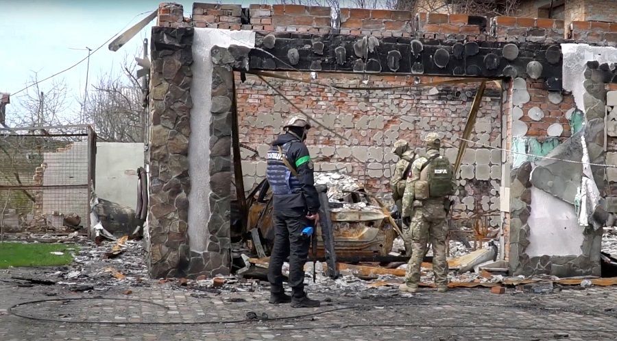 A screen grab shows members of the police and military standing by destroyed buildings and debris, amid Russia's invasion of Ukraine, in Moschun, Kyiv region, Ukraine, 26 April 2022, obtained from a video released 27 April 2022. (YouTube/Andrey Nebitov/Handout via Reuters)