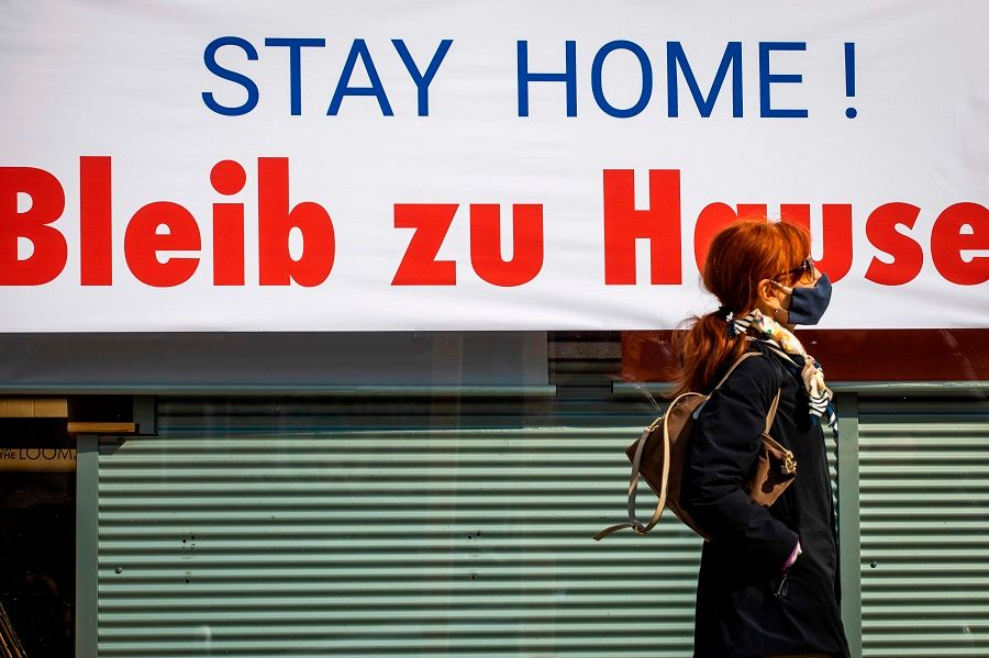 In this photo taken on 28 March 2020, a shopper walks past a print shop in Berlin with a sign advising its customers to stay at home amid the novel coronavirus pandemic. (Odd Andersen/AFP)