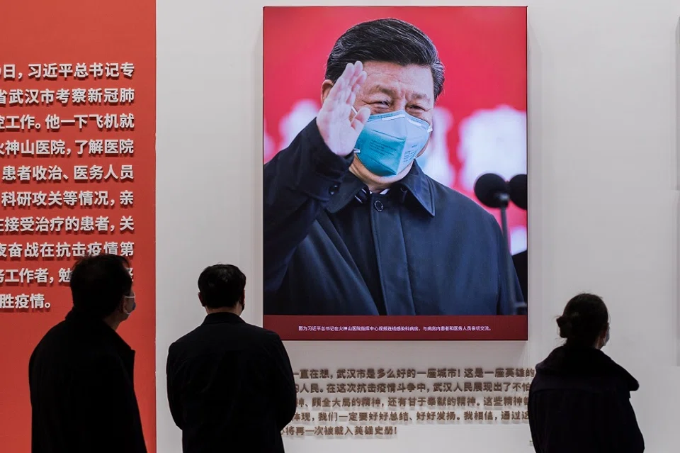 In this picture taken on 15 January 2021, a picture of Chinese President Xi Jinping with a face mask is displayed as people visit an exhibition about China's fight against the Covid-19 coronavirus at a convention centre that was previously used as a makeshift hospital for patients in Wuhan. (Nicolas Asfouri/AFP)