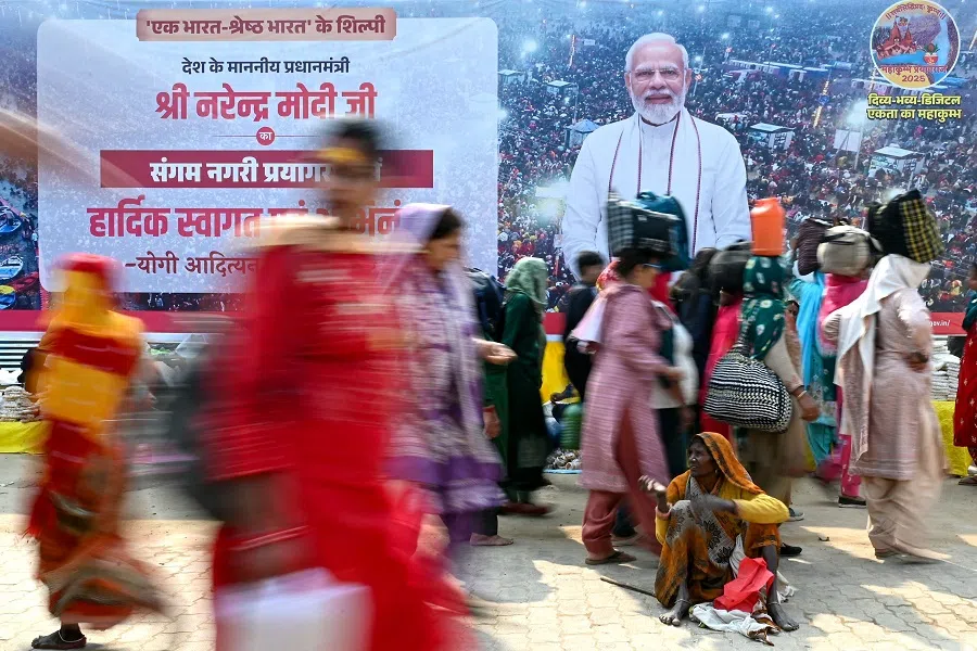 Pilgrims walk past a banner of India’s Prime Minister Narendra Modi ahead of his arrival to take a holy dip at Sangam, the confluence of Ganges, Yamuna and mythical Saraswati rivers during the Maha Kumbh Mela festival in Prayagraj on 5 February 2025.