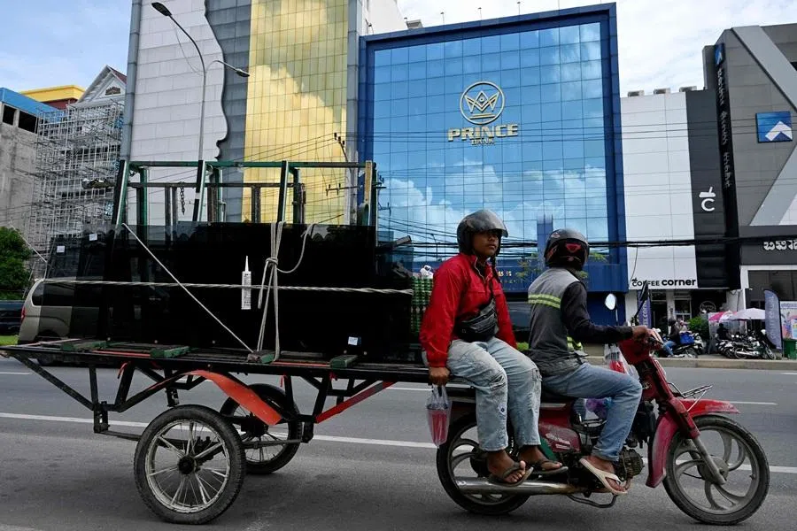 Workers ride their motor-cart loaded past a branch of the Prince Bank in Phnom Penh on 15 October 2025. A Cambodian bank founded by accused scam boss Chen Zhi, who has been indicted by the United States and extradited to China, was ordered liquidated on 8 January 2026, Cambodia's central bank said. (Tang Chhin Sothy/AFP)