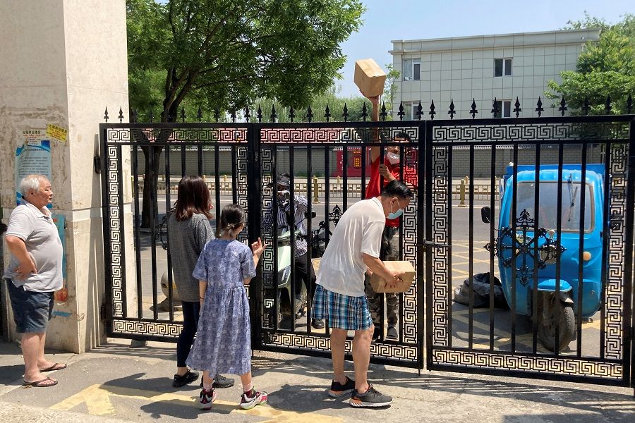 A courier hands parcels through a closed gate of a residential compound where delivery workers are not allowed to enter, amid the Covid-19 outbreak, in Beijing, China, 22 May 2022. (Martin Pollard/Reuters)
