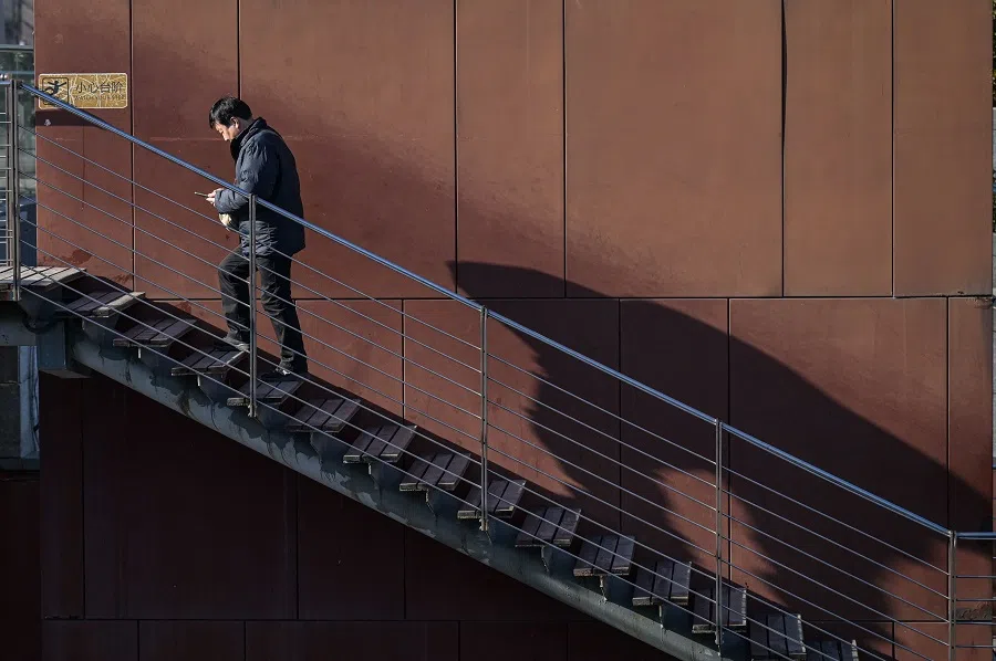 A man walks upstairs as he checks his phone in Beijing on 3 January 2025. (Jade Gao/AFP)