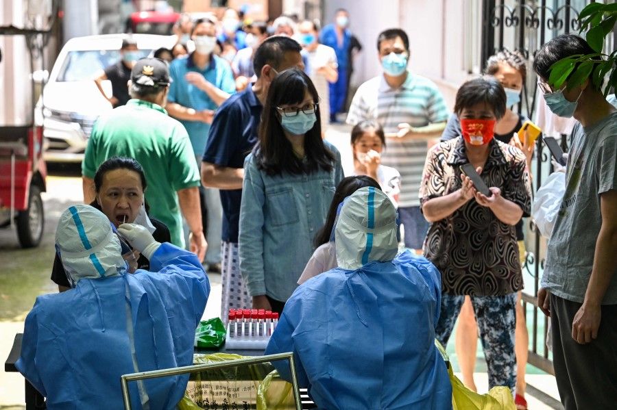 A health worker takes a swab sample from a woman at the entrance of a residential area under Covid-19 lockdown in the Changning district of Shanghai on 11 June 2022. (Hector Retamal/AFP)