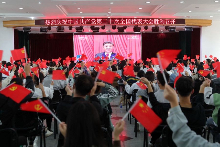 This photo taken on 16 October 2022 shows people waving national flags and Communist Party flags as they watch the opening session of the 20th Chinese Communist Party Congress in Huaibei, in China's eastern Anhui province. (AFP)