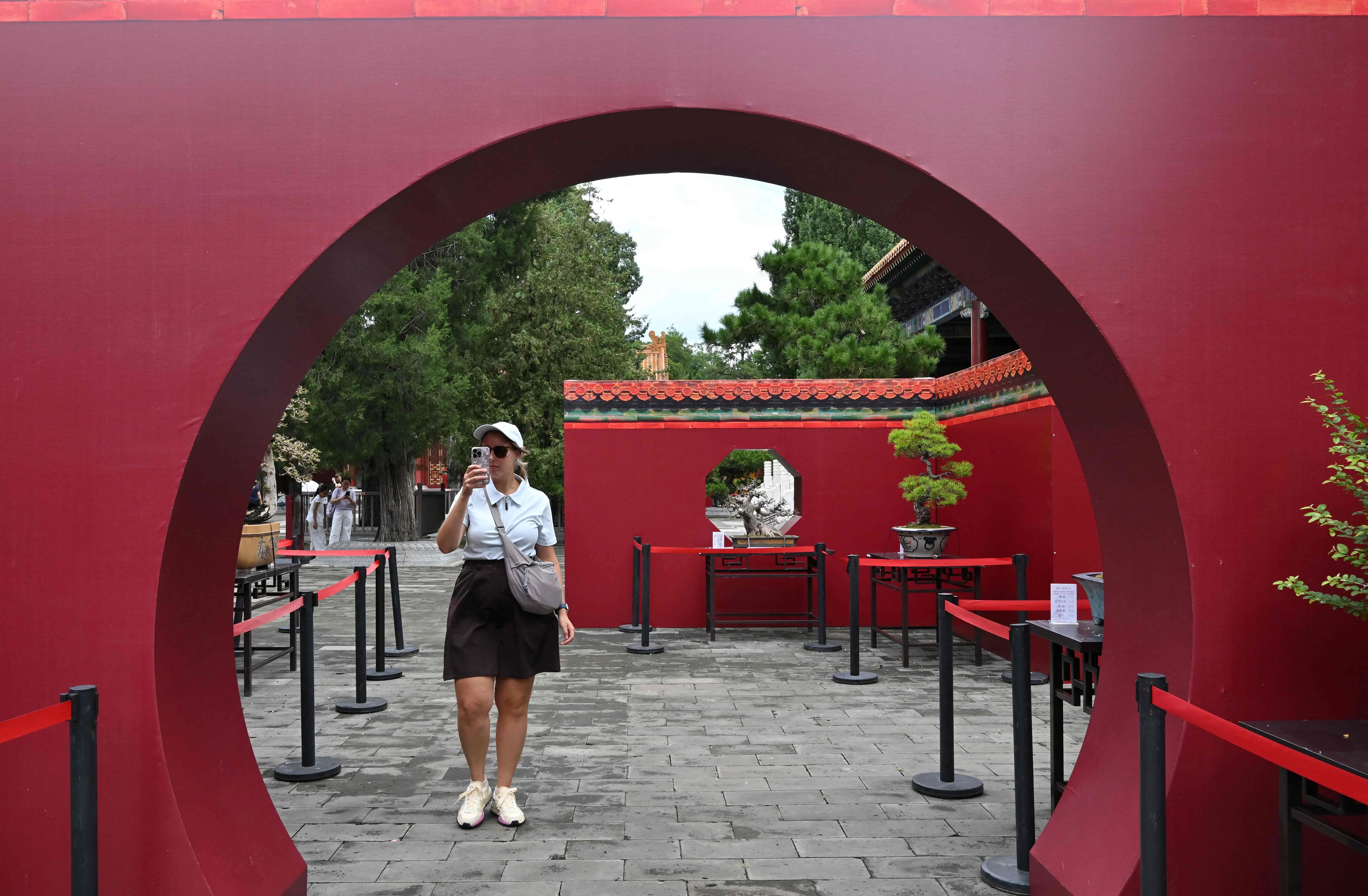 A foreign tourist records with her mobile phone as people visit Jingshan Park, Beijing, on 13 August 2026.