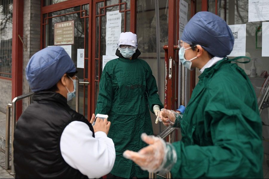 Medical staff wear face masks to protect against the Covid-19 coronavirus as they chat outside a hospital in Beijing on 20 February 2020. (Greg Baker/AFP)