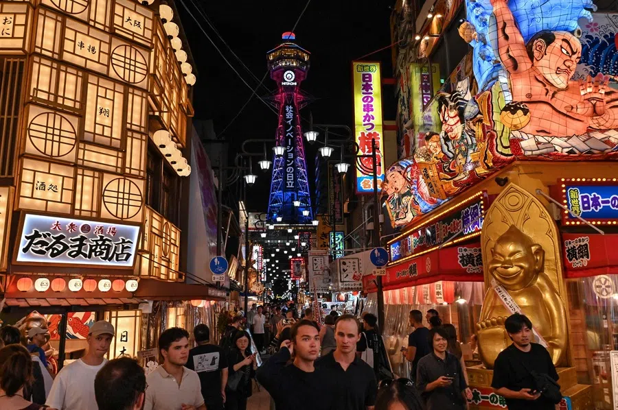 This photo taken on 30 September 2025 shows tourists visiting the main crossroads of the popular Shinsekai area in Naniwa ward as Tsutenkaku Tower looms in the background in Osaka. (Richard A. Brooks/AFP)