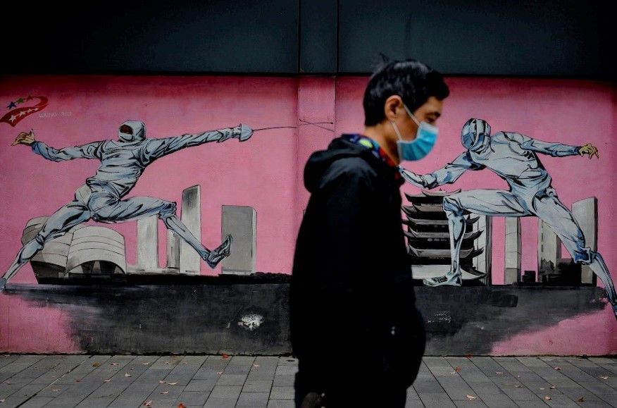 A man wearing a face mask walks past a mural along a street in Wuhan, China, on 2 April 2020. (Noel Celis/AFP)
