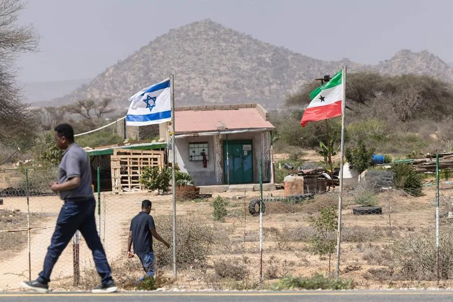 People walk by the flags of Israel and Somaliland flying alongside each other at the entrance to a fruit farm between the capital city of Hargeisa and Port city of Berbera along the highway connecting the two, in Somaliland on 19 February 2026.