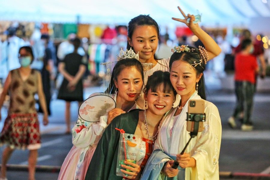This photo taken on 27 August 2020 shows women wearing traditional clothing posing for photos as they visit a night market in Wuhan in China's central Hubei province. (STR/AFP)