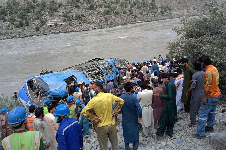 Rescue workers and onlookers gather around a wreck after a bus plunged into a ravine following a bomb explosion, which killed 13 people including nine Chinese workers, in the Kohistan district of Khyber Pakhtunkhwa province, Pakistan on 14 July 2021. (STR/AFP)