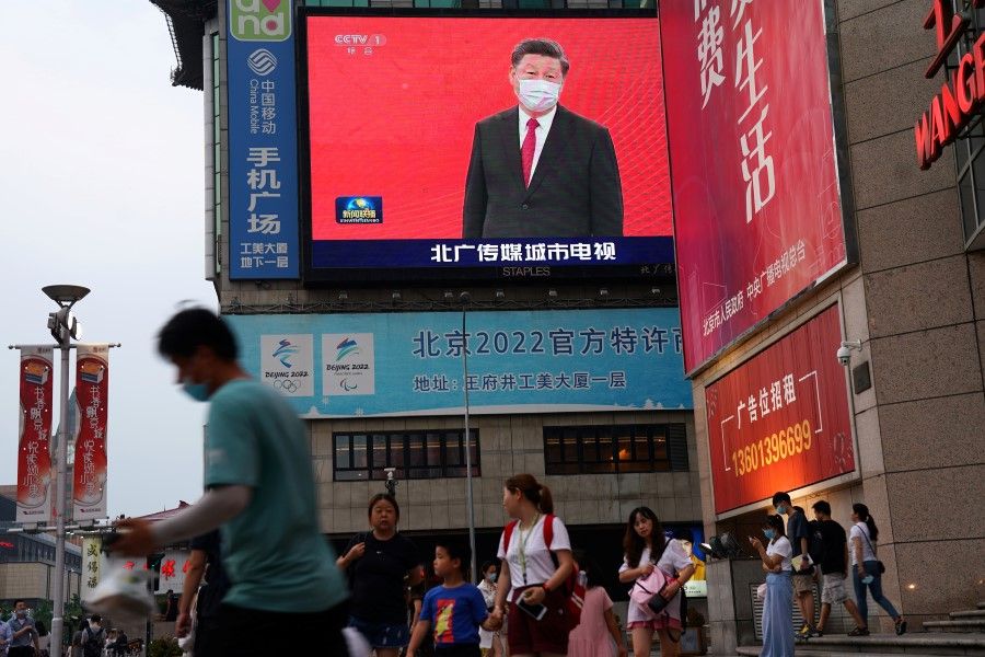 People walk past a giant screen showing a news footage of Chinese President Xi Jinping wearing a face mask, at a shopping area in Beijing, 31 July 2020. (Tingshu Wang/REUTERS)