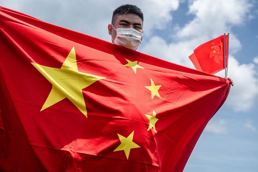 A government supporter wearing a protective mask holds Chinese and Hong Kong Special Administrative Region (HKSAR) flags to celebrate the passage of a national security law in Hong Kong, China, on 30 June 2020. (Lam Yik/Bloomberg)