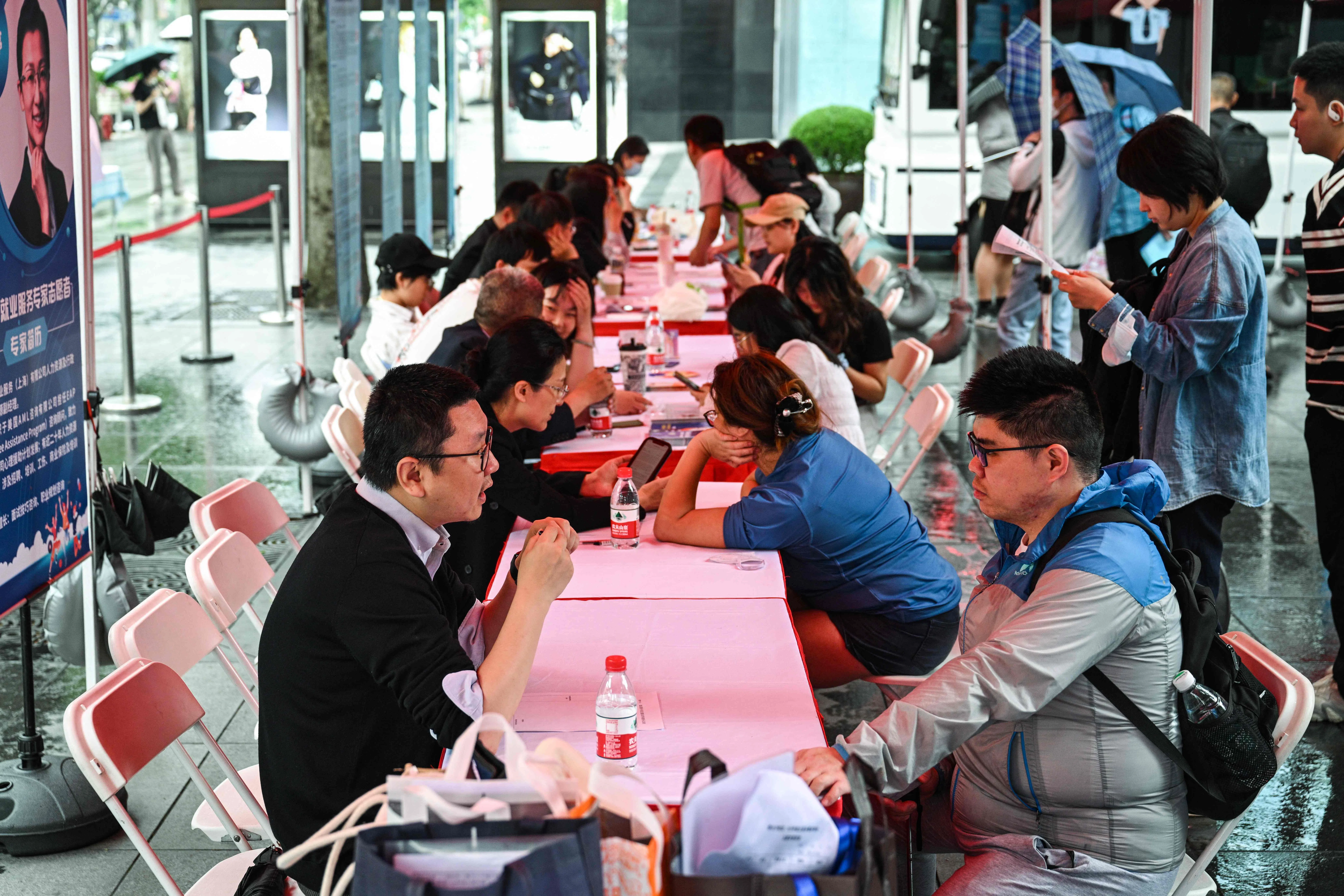 People visit a job fair for soon-to-be graduates in central Shanghai, China, on 31 May 2024, where recruiters sat bored under washed-out tarpaulins as rain and an apparent lack of interest kept potential young employees away. (Hector Retamal/AFP)