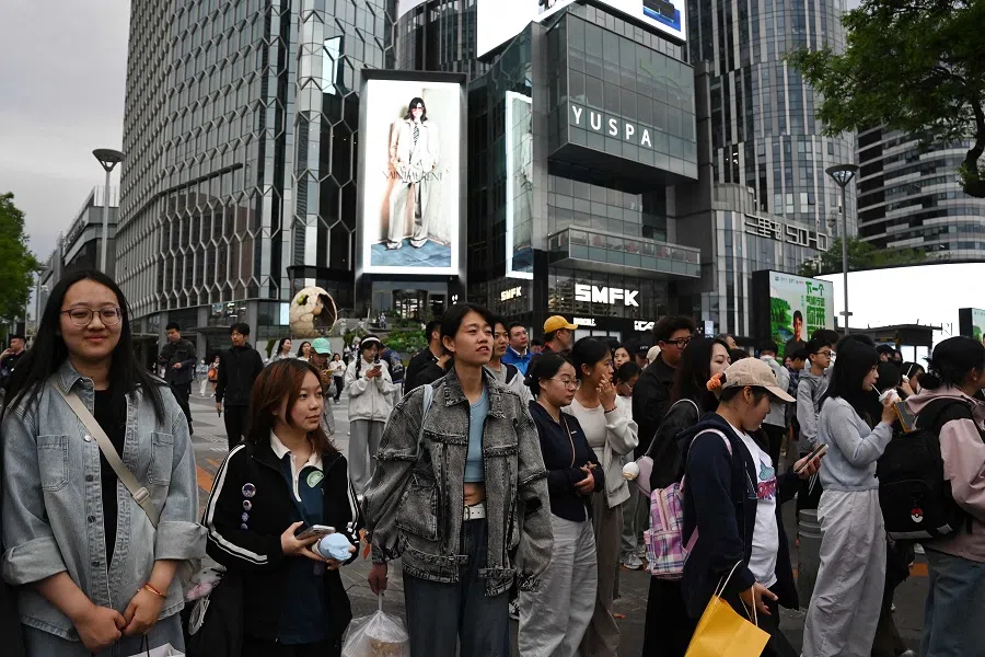 People wait to cross a road outside a shopping mall in Beijing on 2 May 2025. (Greg Baker/AFP)