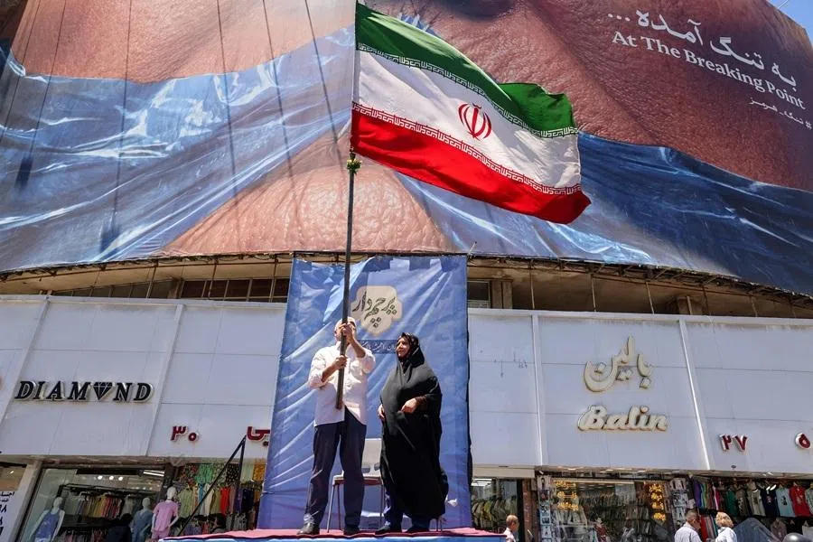 A man raises an Iranian flag as he stands on a podium before a political billboard featuring US President Donald Trump and the Strait of Hormuz along Valiasr Square in Tehran on 26 May 2026.