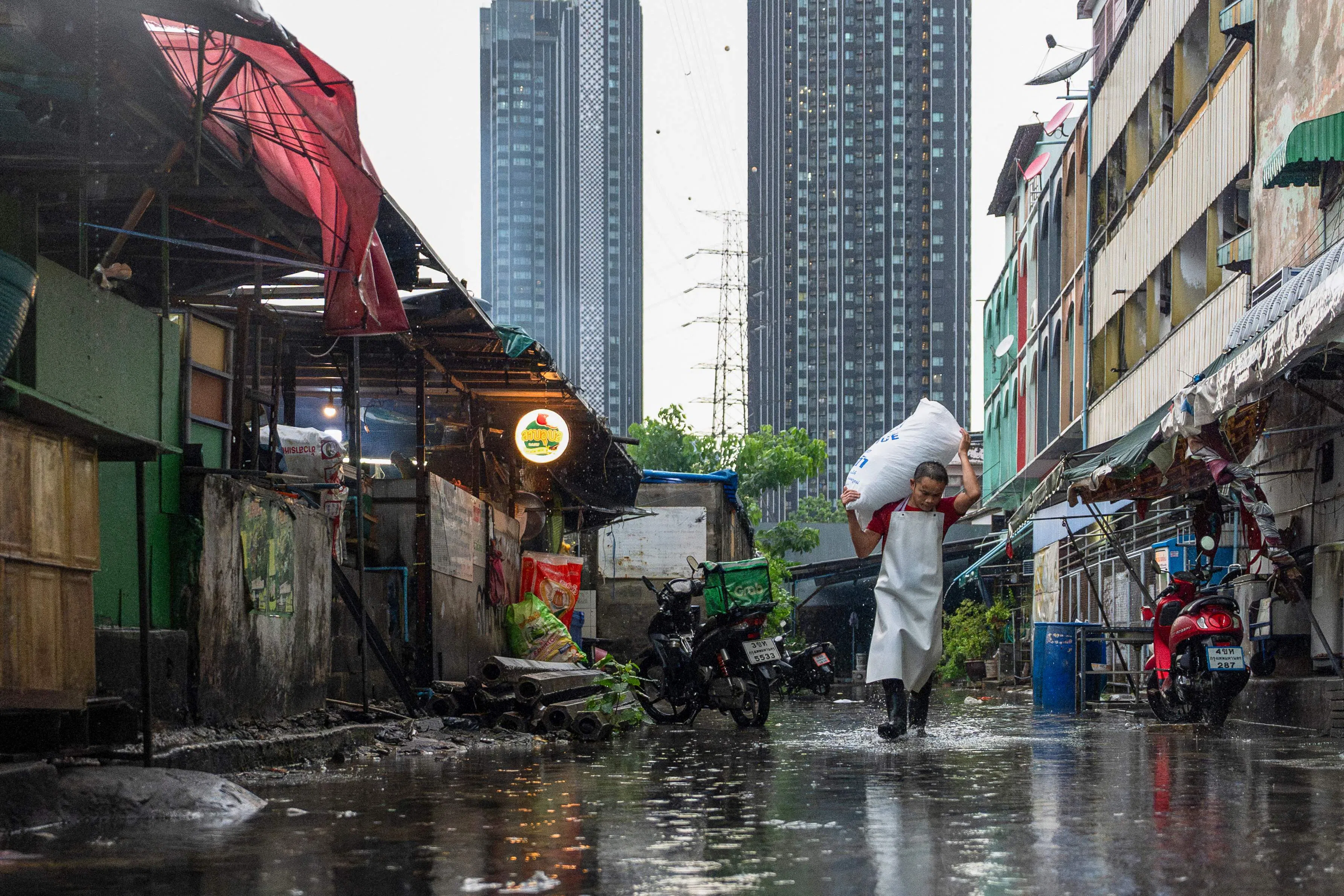 A worker carries a bag of ice through an alley in Bangkok on 21 July 2024. (Chanakarn Laosarakham/AFP)