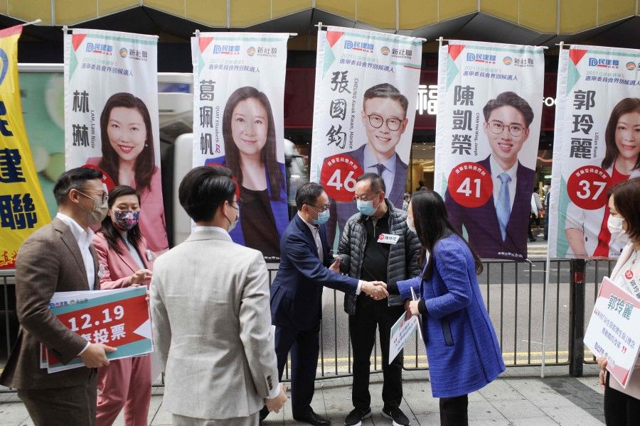 Legislative Council candidates shake hands at a street booth ahead of the 19 December 2021 election in Hong Kong on 16 December 2021. (Bertha Wang/AFP)