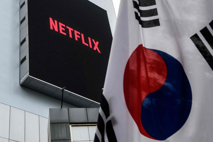 In this photo taken on 7 October 2021, a large digital screen on a building displays the logo of Netflix, producers of the South Korean hit series Squid Game, beyond a South Korean flag hoisted above a pavement in Seoul. (Anthony Wallace/AFP)