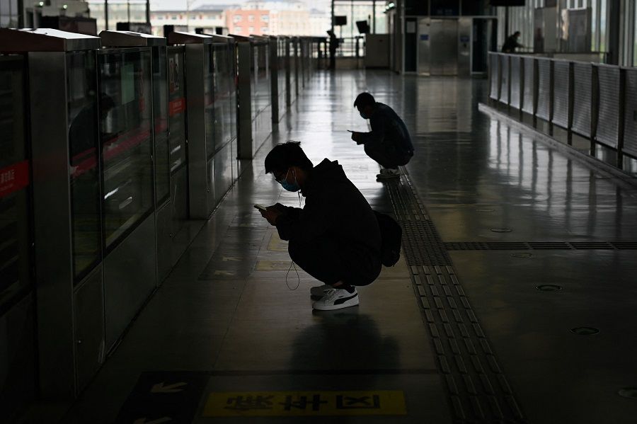 Two men use their mobile phone as they squat waiting for a train at a subway station in Beijing, China, on 26 April 2021. (Wang Zhao/AFP)