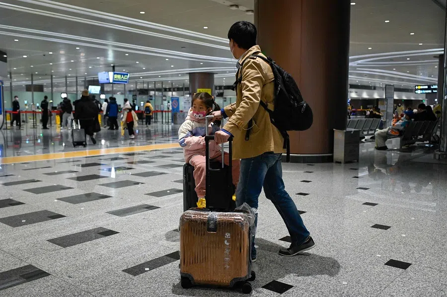A man walks toward the entrance of security check with a child sitting on luggage at Beijing Daxing International Airport in Beijing, China, on 19 January 2023. (Wang Zhao/AFP)