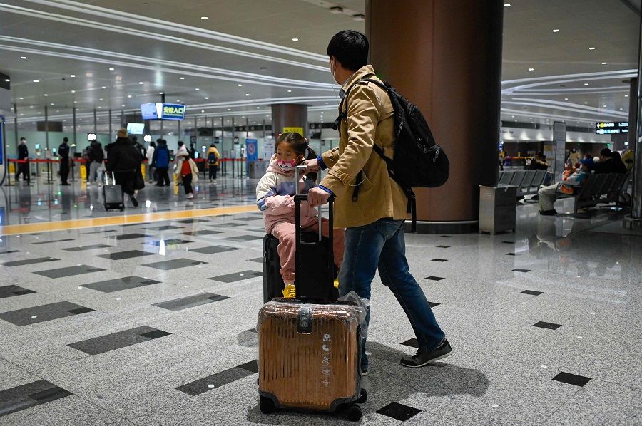 A man walks toward the entrance of security check with a child sitting on luggage at Beijing Daxing International Airport in Beijing, China, on 19 January 2023. (Wang Zhao/AFP)