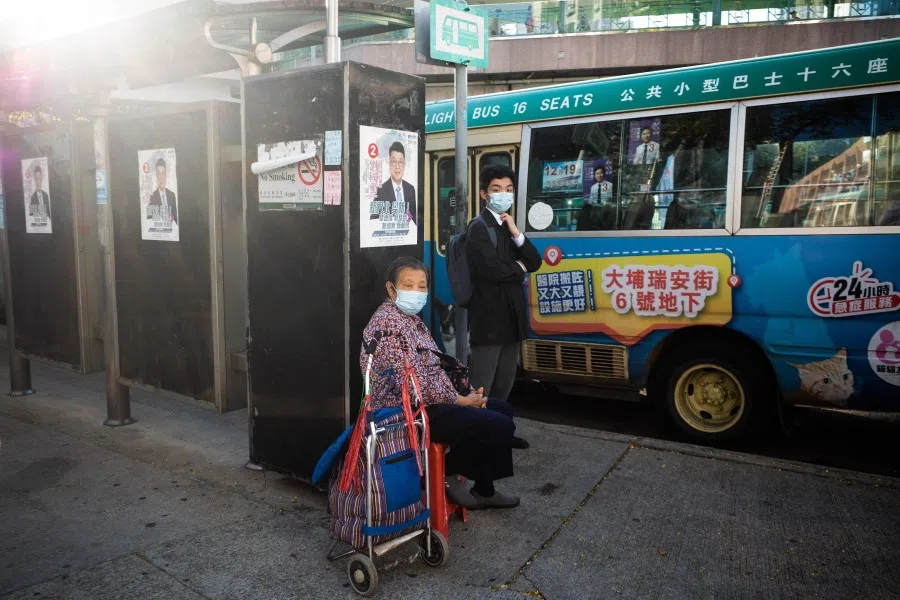 People wait for a bus next to campaign posters for Legislative Council member Edward Lau Kwok-fan, who will run in the upcoming 19 December Legislative Council election, in Hong Kong on 10 December 2021. (Bertha Wang/AFP)