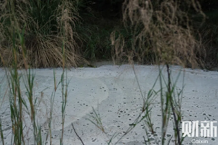Toxic white foam coats the surface of a green river in Longnan city in Ganzhou, China, in March 2022. (Ding Gang/Caixin)
