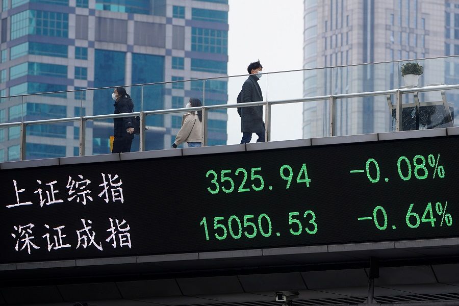 People wearing face masks walk on an overpass with an electronic board showing Shanghai and Shenzhen stock indexes, at the Lujiazui financial district in Shanghai, China, 6 January 2021. (Aly Song/Reuters)